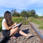 Mujer sentada en unas vías del tren escribiendo