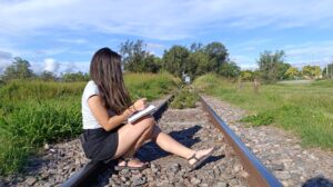 Mujer sentada en unas vías del tren escribiendo
