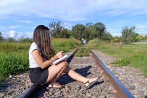 Mujer sentada en unas vías del tren escribiendo