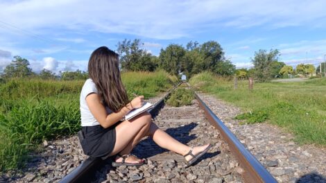 Mujer sentada en unas vías del tren escribiendo
